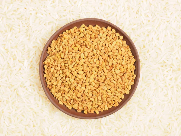 Fenugreek in clay plate. Background from basmati rice. Indian cu — Stock Photo, Image