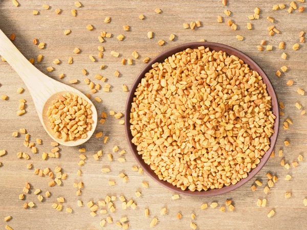 Kahverengi ahşap bir arka planda, kil plaka ve kaşık içinde FenuGreek.. 