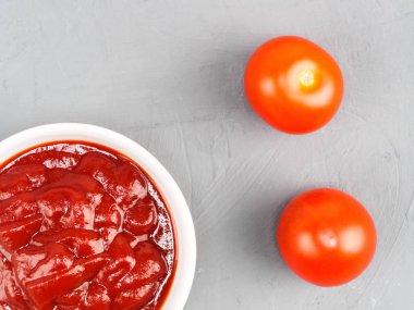 Beyaz bir kaseye domates yapıştırıcı ve gri beton bir torbaya domates.