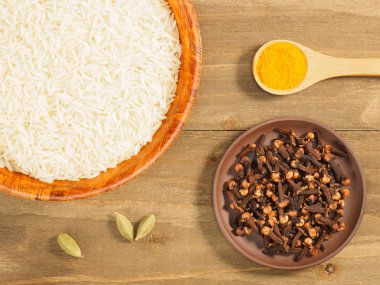 Rice, cloves, turmeric, green cardamom on brown wooden backgroun