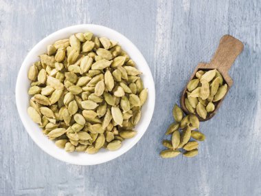 Baharat yeşili kakule (Elettaria kakule) gri beton arka planda ahşap kepçeyle seramik beyaz bir kase içinde. Doğru beslenme konsepti