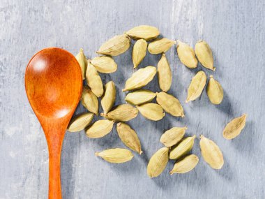 Baharat yeşili kakule (Elettaria kakule) kahverengi ahşap kaşık ve gri beton arka plan yakın plan. Modern eczacı, naturopati ve ayurveda kavramı