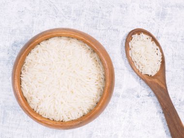 Kahverengi ahşap kasede Basmati pilavı ve beyaz beton arka planda kaşık.