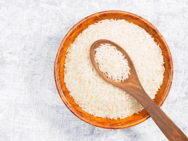 Indian long grain Basmati rice in brown wooden bowl and spoon on white concrete background. Indian cuisine, ayurveda, naturopathy concept