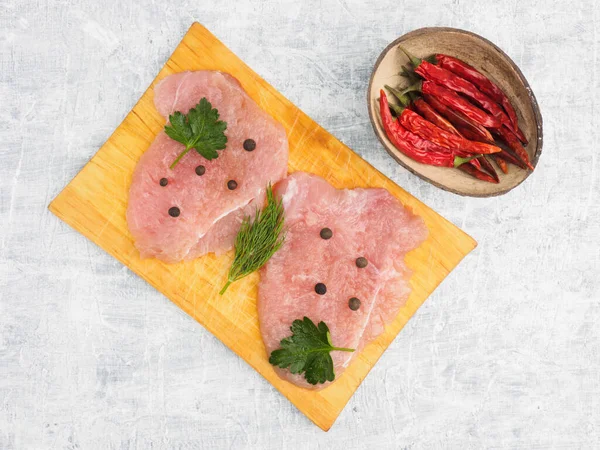 Sliced pieces of meat turkey game filet on a wooden cutting board, herbs, allspice, red chili on a white concrete background. Healthy eating concept