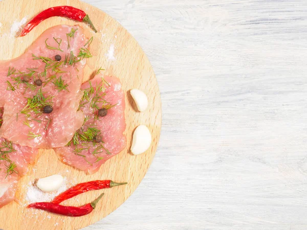Sliced pieces of meat turkey game filet, fennel, garlic, allspice, red chili pepper on wooden cutting board on white wooden background. Healthy eating concept