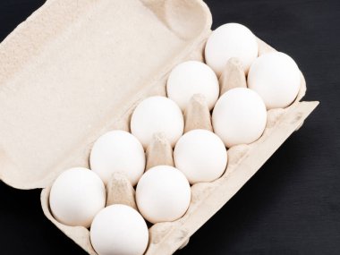 Siyah ahşap arka planda paket başına çiğ beyaz tavuk yumurtası. Sağlıklı beslenme ve organik gıda konsepti