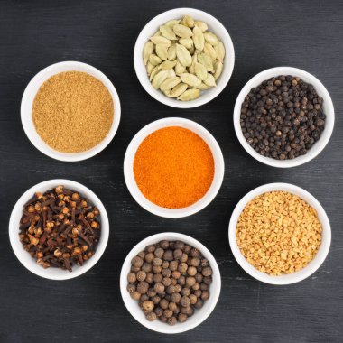 Baharat yeşili kakule, kırmızı biber, karabiber, çemen otu, karanfil, tüm baharatlar, beyaz seramik kasede siyah ahşap arka planda masala tozu. Sağlıklı beslenme ve organik gıda konsepti