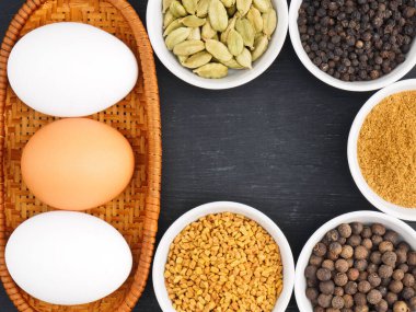 Çiğ tavuk yumurtası, karabiber, masala tozu, baharat, çemen otu, siyah ahşap arka planda yeşil kakule. Çırpılmış yumurta veya omlet yapmak için gerekli malzemeler. Organik gıda konsepti