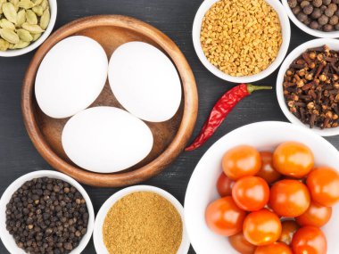 Çiğ tavuk yumurtaları, karabiber, masala tozu, çemen otu, yeşil kakule, acı kırmızı biber, karanfil, siyah ahşap zemin üzerinde domates. Çırpılmış yumurta veya omlet yapmak için gerekli malzemeler. Organik gıda konsepti