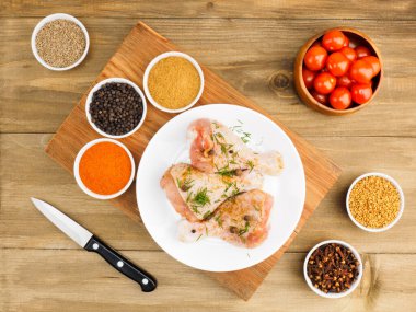 Beyaz seramik tabakta çiğ tavuk budu, bıçak, domates, baharat seti kırmızı biber, masala, karabiber, kimyon, çemen otu, rezene. Sağlıklı yeme kavramı