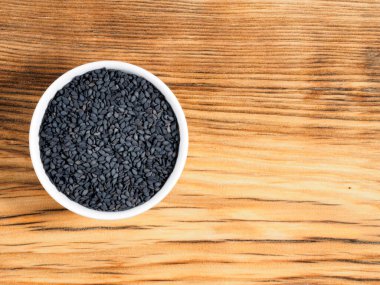 Kahverengi ahşap arka planda beyaz kasede siyah kimyon ve fotokopi alanı. Sağlıklı beslenme, ayurveda, naturopati konsepti