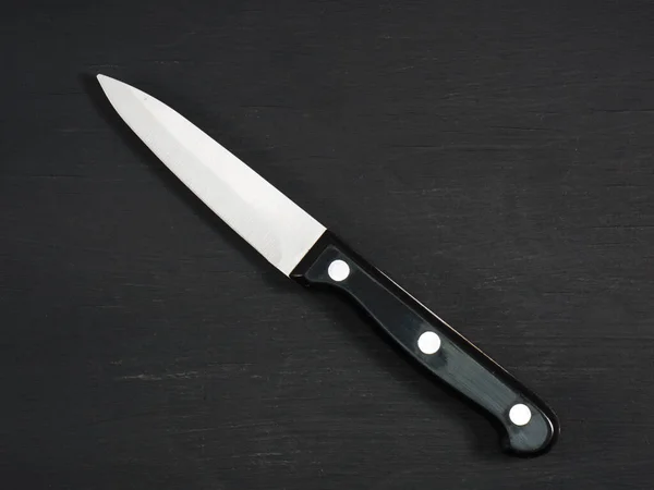 Medium sharp kitchen knife with black handle on a black wooden board. Healthy eating, recipe concept