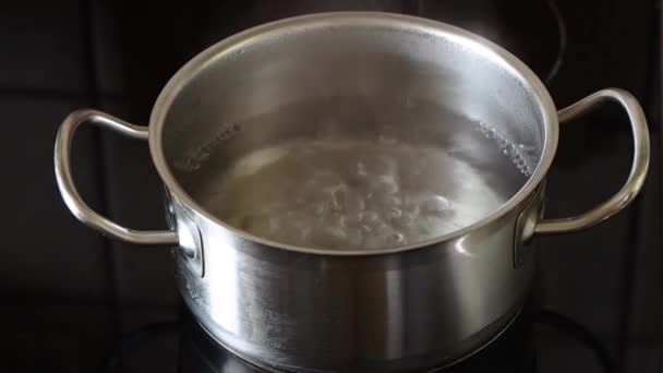 ストーブの上にステンレス製のパン スプーンで沸騰した水にオートミールフレークを追加します 料理のコンセプト — ストック動画