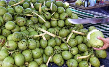 Çiftçi pazarında büyük palalı genç hindistan cevizi kesen yerel bir adam.