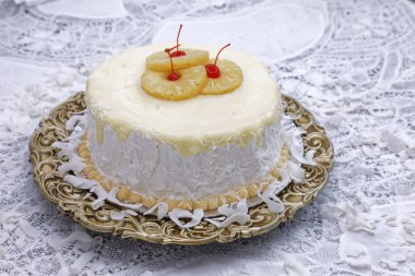 Ananas dilimleri ve kahverengi tabakta kirazlarla süslenmiş beyaz hindistan cevizi kremalı pasta.