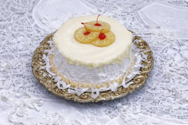 Ananas dilimleri ve kahverengi tabakta kirazlarla süslenmiş kabarık ve nemli hindistan cevizli kek.