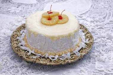 Ananas dilimleri ve kahverengi tabakta kirazlarla süslenmiş beyaz hindistan cevizi kremalı pasta.