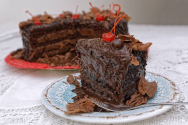 Bir dilim çikolatalı pasta ve çatalla süslenmiş kirazlarla süslenmiş.