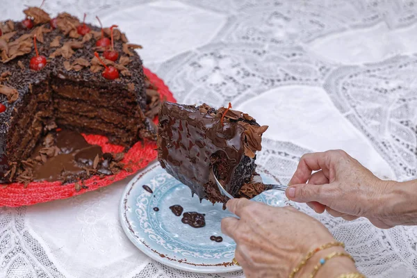 女性の手はチェリーとブルーソーサーに茶色のチョコレートペストリーケーキの一部を取ります — ストック写真