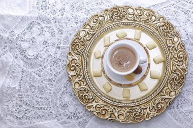 Sıcak bir fincan kahve beyaz ve altın tabaklar üzerinde bisküvi.