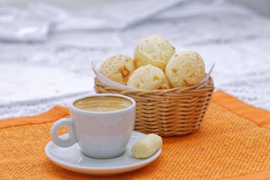 Sıcak, koyu kahve fincanı, peynirli çörekler sepsiyonda, mutfak arka planında turuncu peçete.