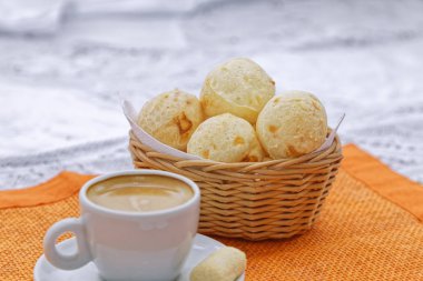 Sıcak, koyu kahve fincanı, peynirli çörekler sepsiyonda, mutfak arka planında turuncu peçete.