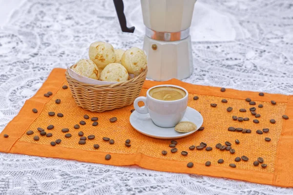 cheese buns in basket with strong coffee cup and coffee kettle on orange napkin with coffee beans