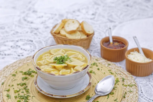 fresh chicken meat dumplings in broth with basket of bread slices and sauces