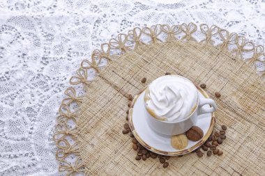 Krem şantili bir fincan kapuçino ve kahve çekirdekli beyaz tabakta bisküvi.