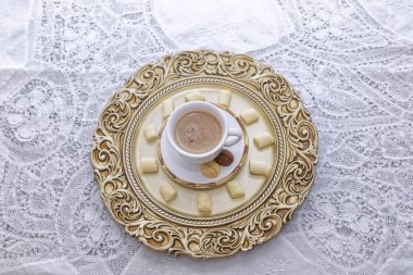 Sıcak bir fincan kahve beyaz ve altın tabaklar üzerinde bisküvi.