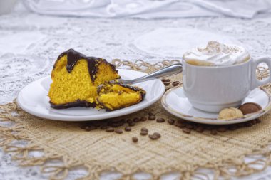 Bir parça fırında limonlu kek, siyah çikolatalı ve beyaz tabakta bisküvili kapuçino.