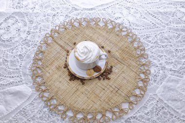 Krem şantili bir fincan kapuçino ve kahve çekirdekli beyaz tabakta bisküvi.