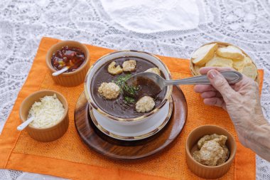 İnsan eli kaşıkla domates çorbası yerken bir sepet ekmek dilimleri, aperatifler ve soslar