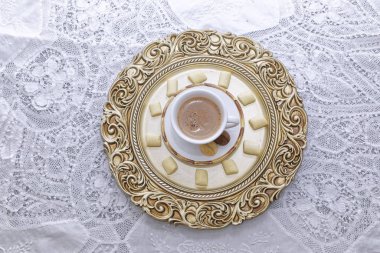 Sıcak bir fincan kahve beyaz ve altın tabaklar üzerinde bisküvi.