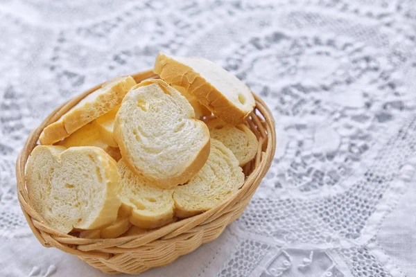 Beyaz mutfak masasının üzerinde dilimlenmiş beyaz ekmek bulunan ahşap sepet.