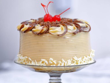 Tereyağlı kremalı beyaz çikolatalı pasta ve cam tabakta kirazlar.