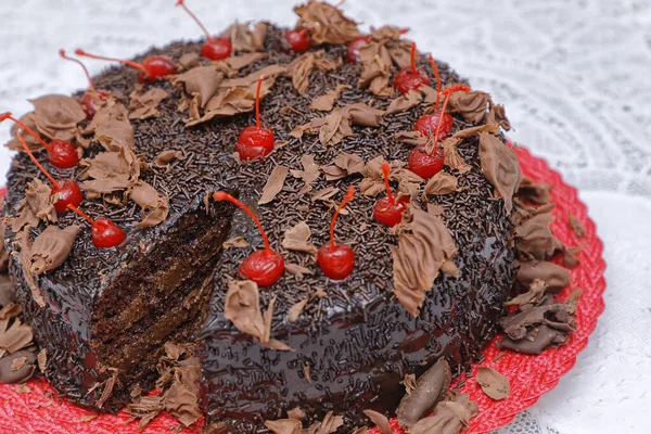 焼きたてのチョコレートケーキにココアパウダーのグレーズとチェリーを赤皿に飾り — ストック写真