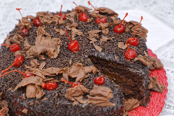 焼きたてのチョコレートケーキにココアパウダーのグレーズとチェリーを赤皿に飾り — ストック写真