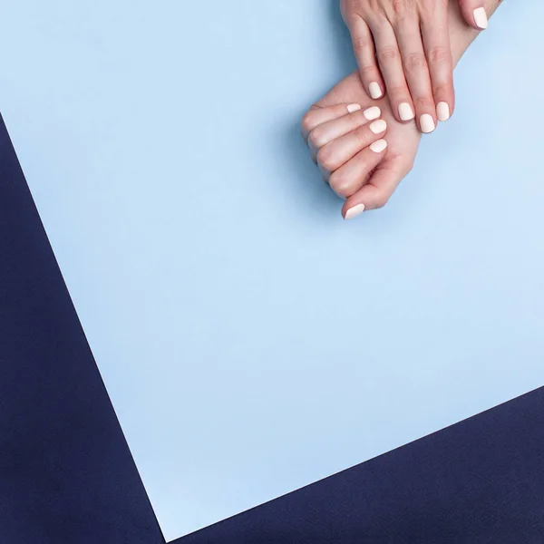 Belles mains féminines avec une manucure classique mate sur fond bleu — Photo