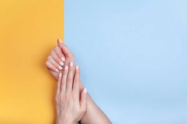 Belles mains féminines avec une manucure classique mate sur fond bleu-jaune — Photo
