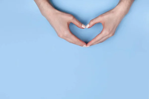 Kobiece dłonie pokazują symbol serca na jasnoniebieskim tle. Miejsce na tekst, miejsce na kopię — Zdjęcie stockowe