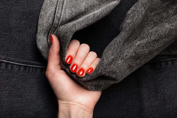 Une main avec une manucure rouge tient un denim gris . — Photo