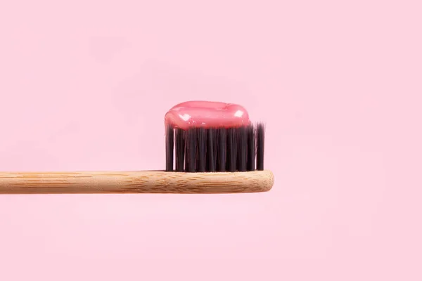 Drewniana szczoteczka do zębów z różową pastą zbliżenie na różowym tle — Zdjęcie stockowe