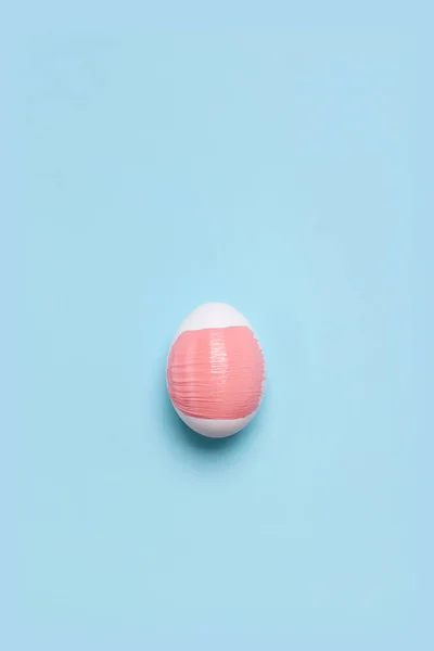 Un œuf de poulet blanc avec frottis rose sur le fond bleu clair — Photo