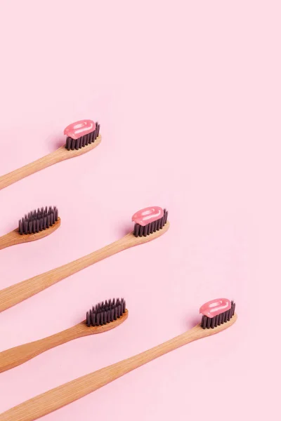 Una fila de cepillos de dientes de madera sobre un fondo rosa — Foto de Stock