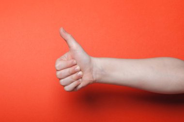 Çocuk eli kırmızı arkaplanda başparmağını gösteriyor