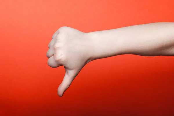 Το χέρι του παιδιού δείχνει τον αντίχειρα κάτω στο κόκκινο φόντο — Φωτογραφία Αρχείου