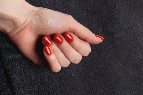 Une main avec une manucure rouge sur fond denim gris — Photo