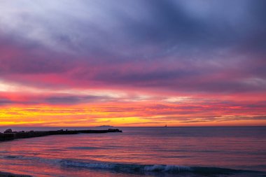 Günbatımında Toskana 'da Akdeniz' de bir rıhtım. Arka planda bir ada ve yelkenli var.